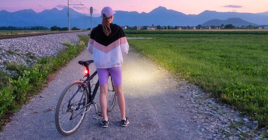 A woman stands next to her bicycle on a gravel road in a rural area.